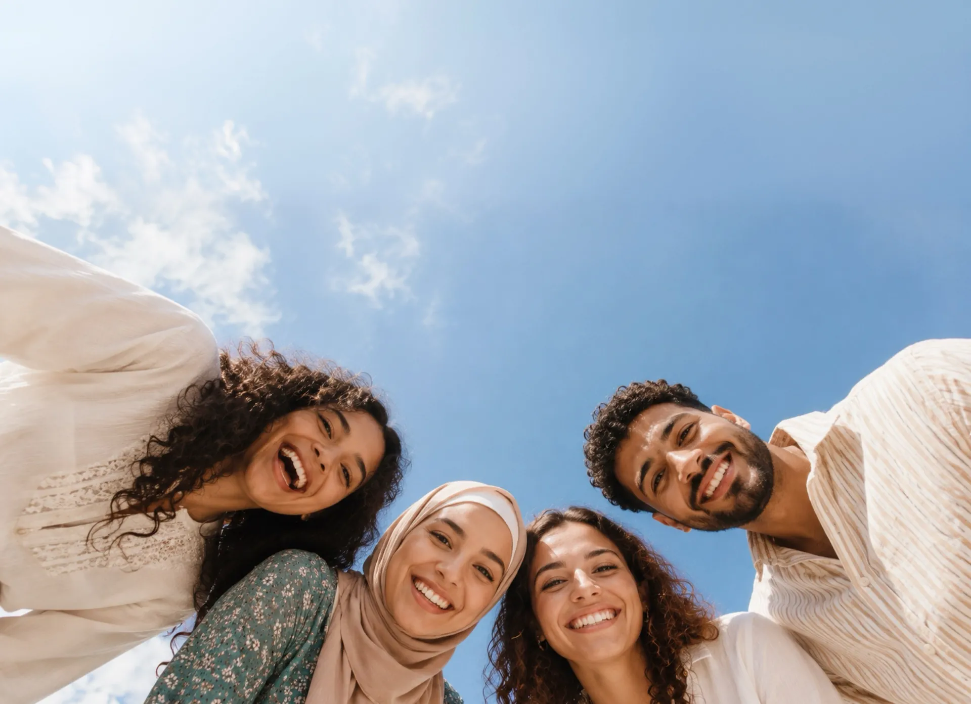 Four friends huddled together smiling down at the camera against a blue sky